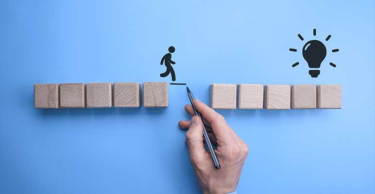 Male businessman’s hand drawing a connecting line between two sets of wooden blocks for a silhouetted man to walk across.