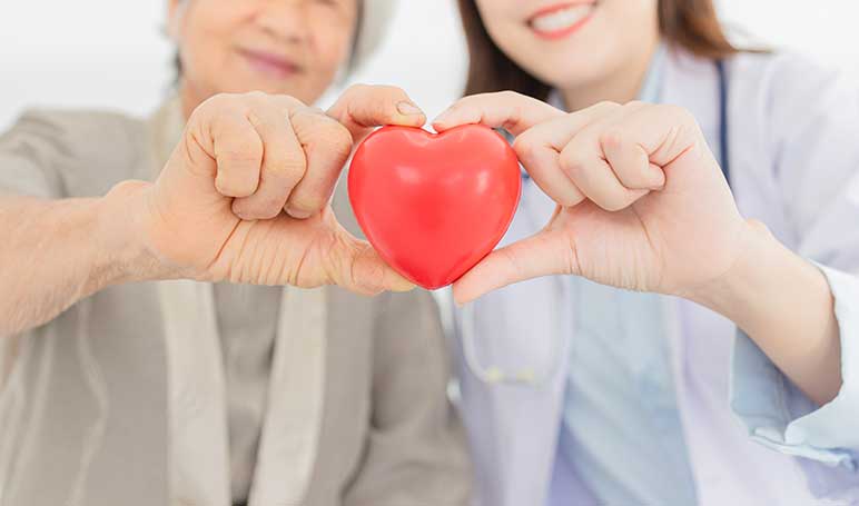 close-up of hands holding red heart, young female Asian doctor and older female patient