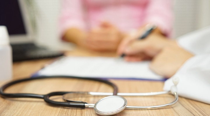 Doctor writes prescription with stethoscope in foreground.